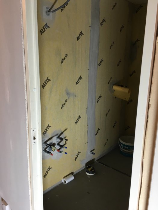 Badrum under renovering med väggisolering och rörinstallationer synliga före kakelsättning.