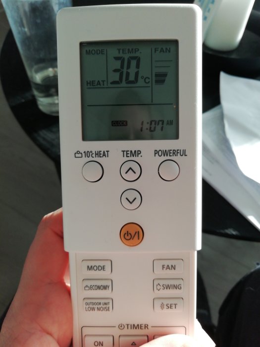 Hand håller en vit AC-fjärrkontroll visande 30°C och flera funktioner.