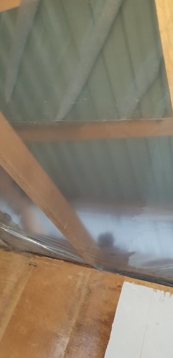 Utsikt inifrån en arbetsbod under renovering, visar träbjälkar och plåttaket ovanför.