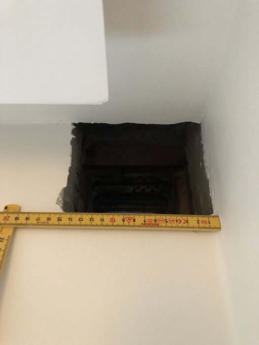 Fyrkantigt hål i en vit vägg med måttband som visar dimensionerna ca 150x120 mm, tidigare del av ventilation.