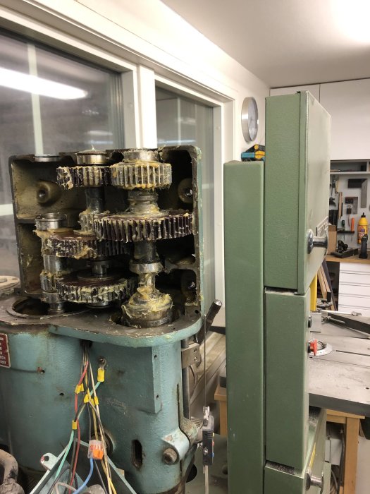 Pillar drill with open gear housing showing greased gears and internal components during service.