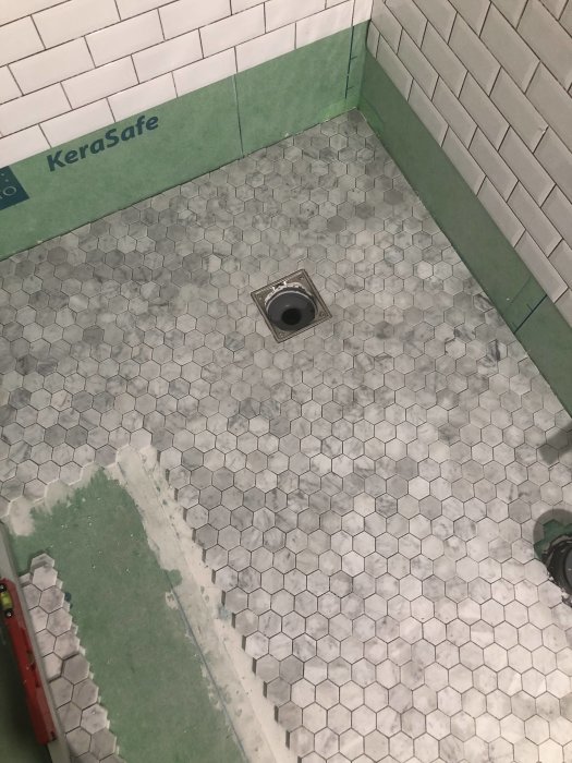 Halvlagt, hexagonalt kakelgolv i badrum med öppen golvbrunn och väggar förberedda för kakling.