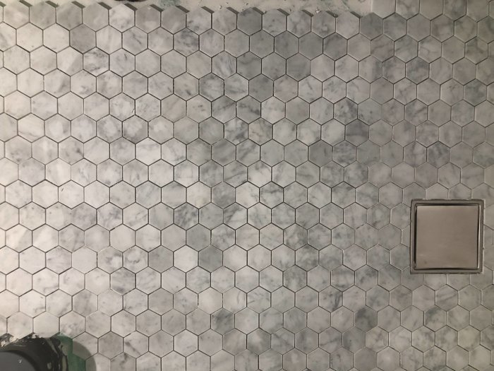 Halvlagt mosaikklinkergolv i badrum med utklipp för golvbrunn och symmetriskt mönster.