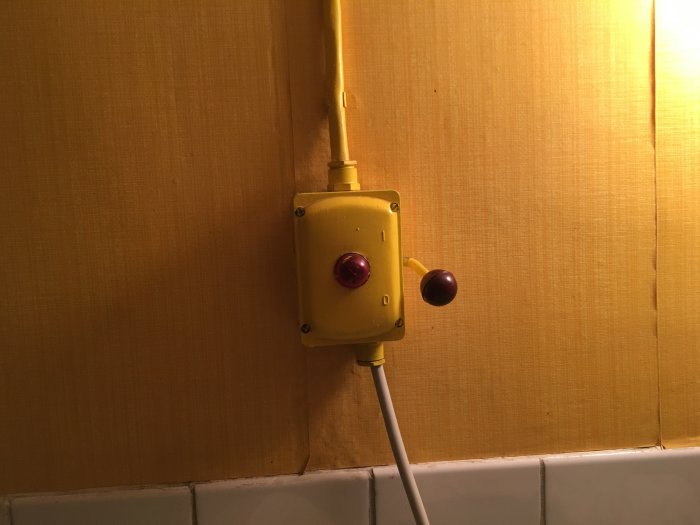 Gammal gul strömbrytare på vägg med tapeter, kabel och rattar.