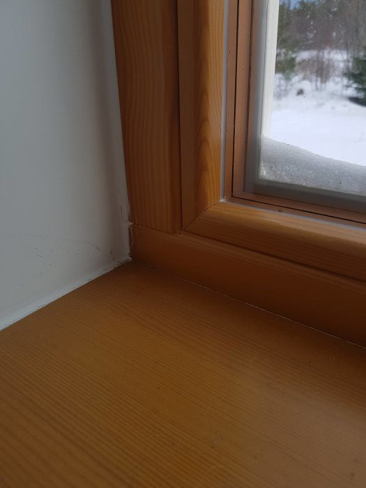 Detaljbild av träfönster och fönsterbräda inomhus med utsikt till snöigt landskap.