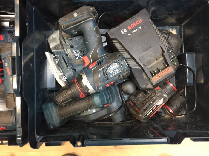 En öppen verktygslåda fylld med olika Bosch batteriverktyg och en batteriladdare, trånga och ostrukturerade förhållanden.