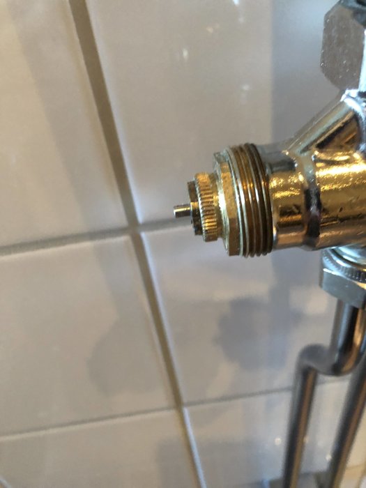 Närbild av en termostatventil med en synlig stift som är delvis utskjuten mot en kakelvägg.