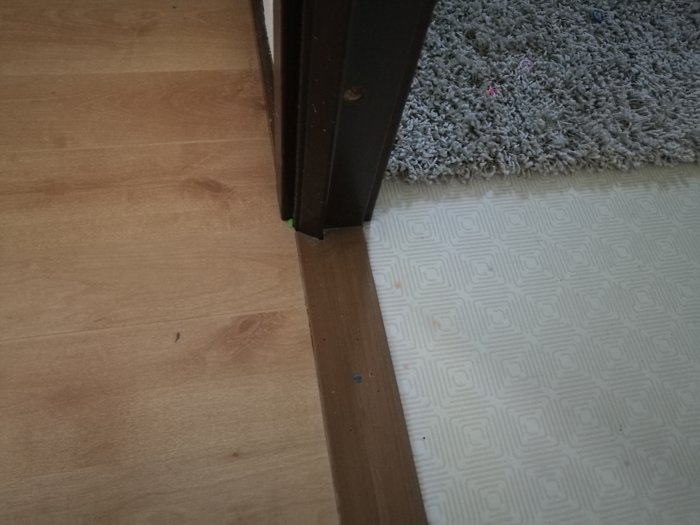 Övergång mellan laminatgolv och plastmatta vid en dörrtröskel inomhus.