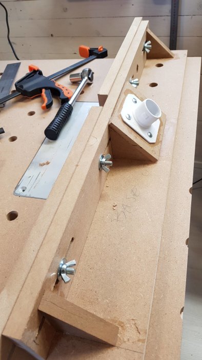 DIY-adapter för spånhantering fastskruvat på arbetsbänk med slanganslutfäste, verktyg och träbitar.