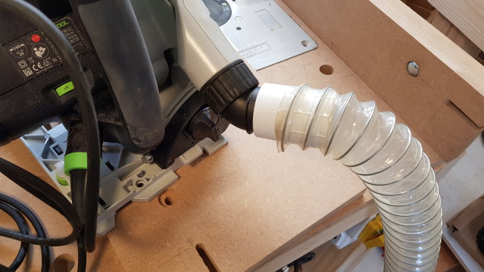 En sugslang från Jula ansluten till en cirkelsåg med ett 3D-printat fäste för spånhantering i en verkstad.