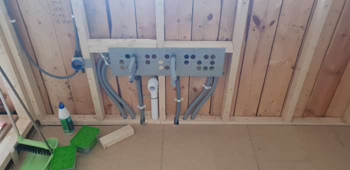 Installation av 50 mm avloppsrör och fästen på vägg med 70 mm reglar, samt sopset i förgrunden.