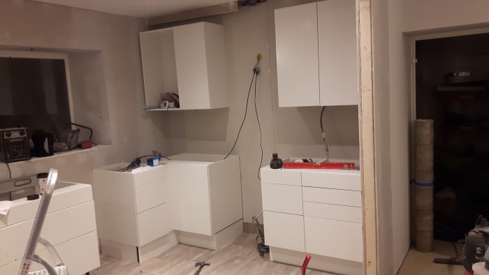 Kök under renovering med vita skåpsstommar och diskmaskin, trånga utrymmen och elinstallationer synliga.