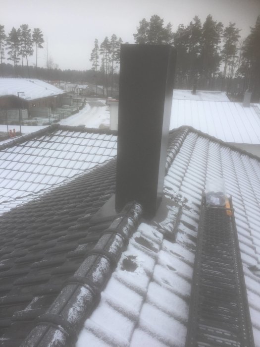 Nyinstallerad svart skorsten på snötäckt tak mot disigt landskap.