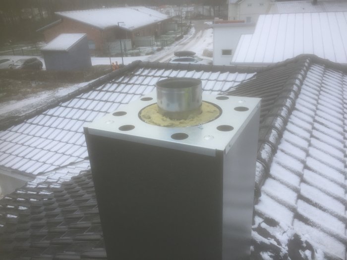 Nyinstallerad kamininsats på tak med snötäckt skorsten och svenskt villaområde i bakgrunden.