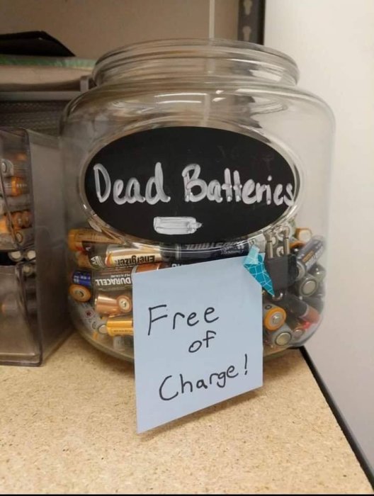 Glasburk full med använda batterier märkt "Dead Batteries", lapp med texten "Free of Charge!