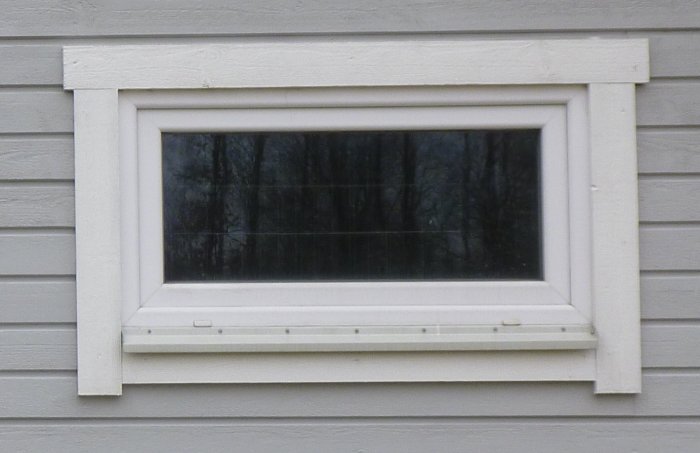 Kompositfönster monterat på en ljusgrå trävägg med synlig vit omramning och underkant som öppnas för vädring.