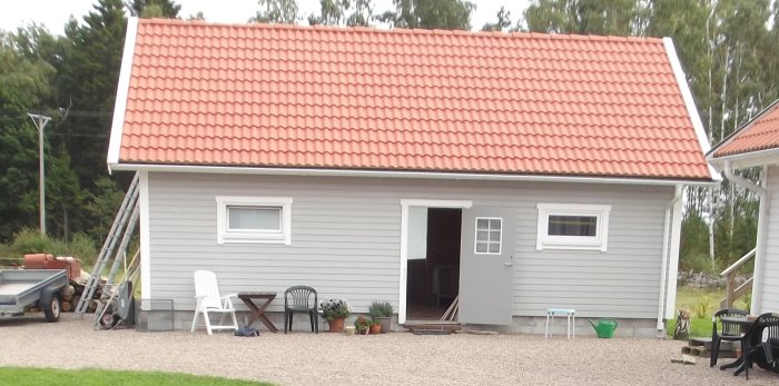 Ett gråmålat stall med rött tegeltak och vita kompositfönster som är jämnt fördelade på längsidorna.