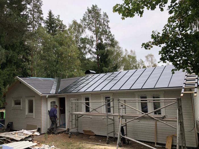 Renoverad suteräng sommarstuga med nytt plåttak och fasadpanel, ställningar utanför.