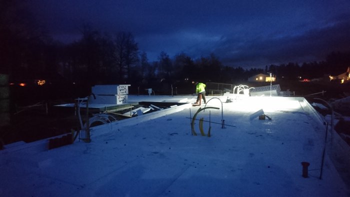 Person arbetar på husgrund med isolering och VVS i gryningen, byggarbetsplats med snö.