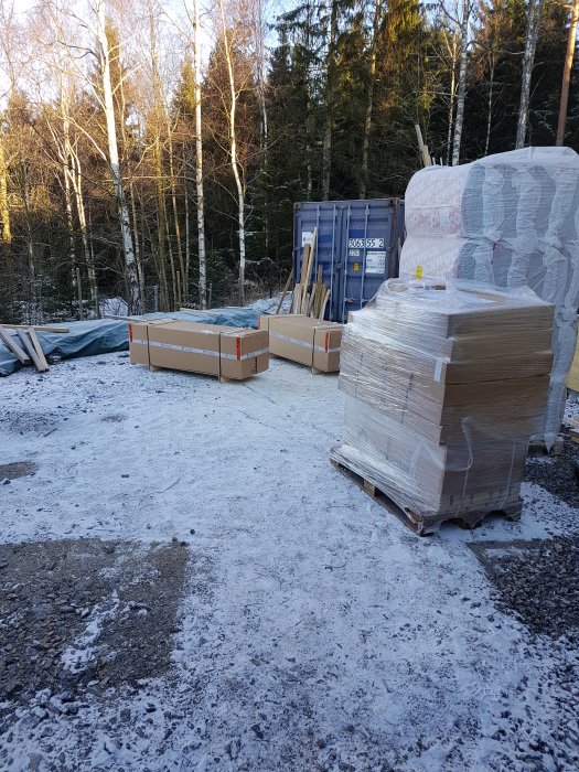 Golvspån i förpackningar på en byggplats med snö, väntande på montering.