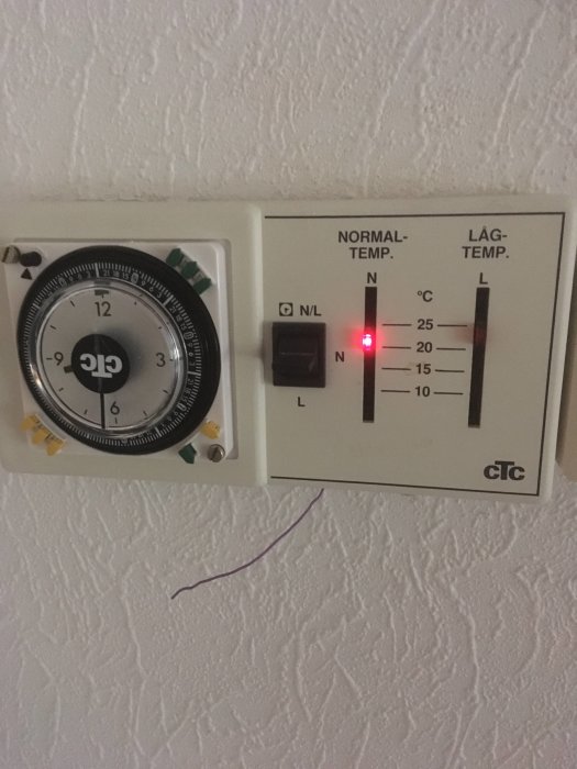 Termostat med ur och reglage för normal och låg temperatur, och en lila ledning utan koppling hänger nedanför.