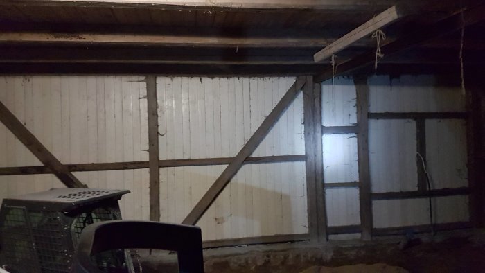 Gamla träbjälkar och vitmålade plankor inuti ett mörkt garage under renovering.