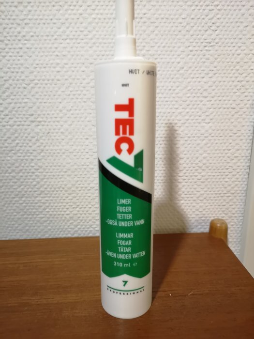 Flaska med TEC 7 fogmassa står mot en texturerad vit vägg.