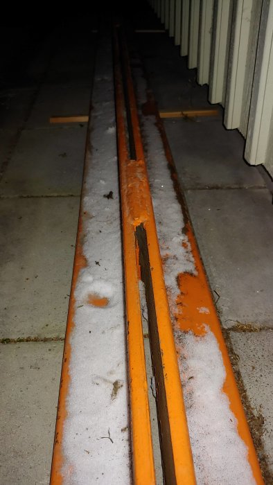 Lång orange balk med ovanligt format och 12mm godstjocklek, liggandes på snötäckt mark.