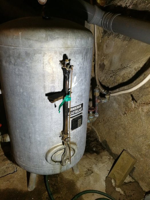 En gammal hydrofor med ett vattenståndsmätarrör där den övre muttern spruckit och med tecken på slitage och korrosion.