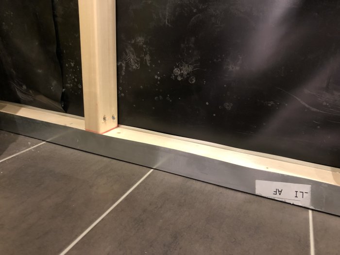 Detaljbild av golv där kakel möter trälist och svart fuktspärr vid en vägg i ett pågående byggprojekt.