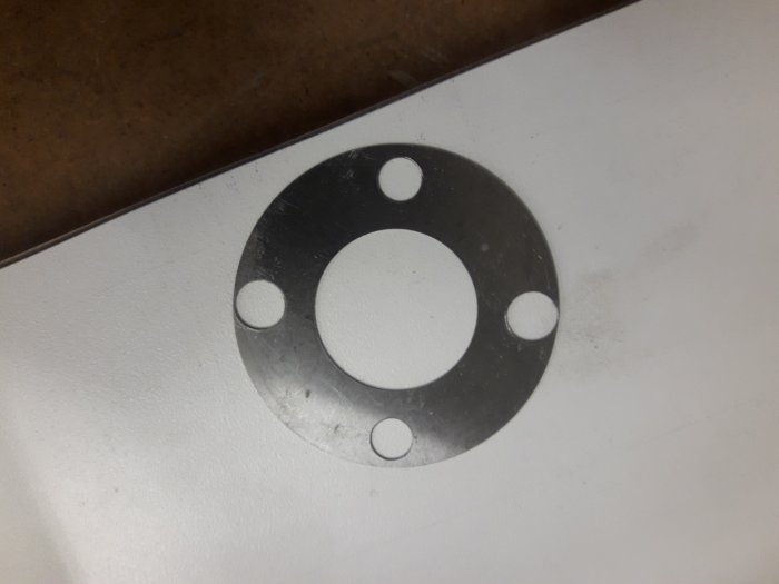 Shim med nyligen borrade hål nära kanten på den tunna metallplåten.