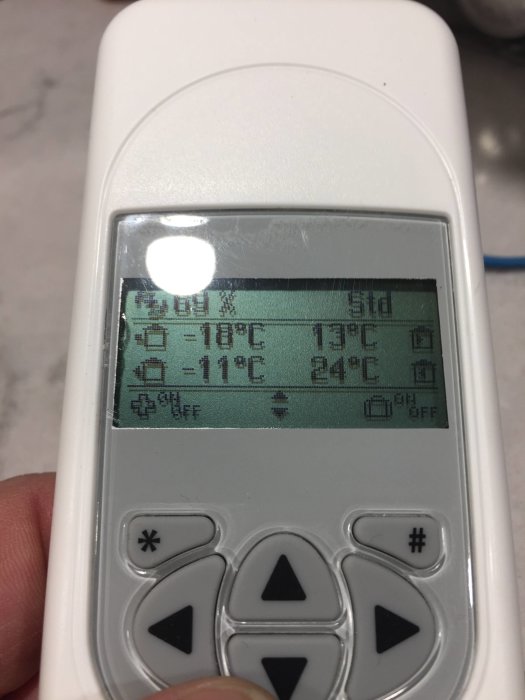 Närbild på en fjärrkontroll som visar temperaturen, -11°C för avluften och ställningar för Heru 100 ventilationssystem.
