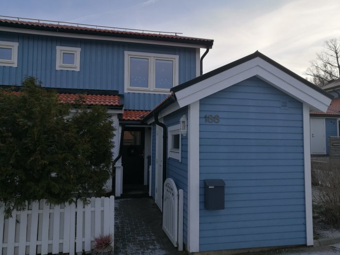 Blått radhus med komplexa takvinklar och ett förråd med anslutande tak vid ingången.