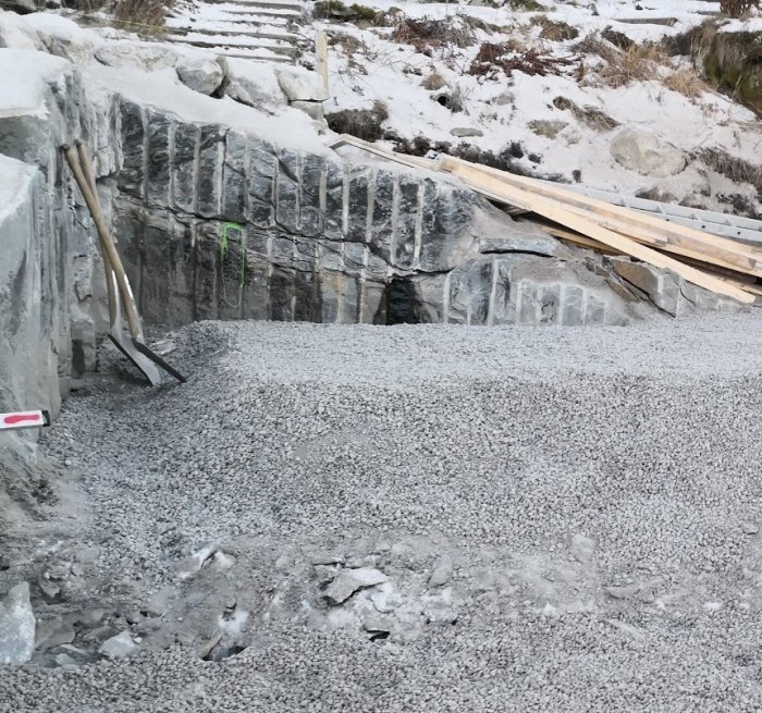 Stödmur med grusplanering och spricka i berg varifrån vatten rinner under bygggrund.