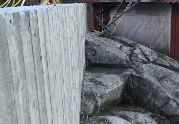 Bild på en stödmur och exponerat berg med synlig vattenrinning, en del av byggarbetsplats.