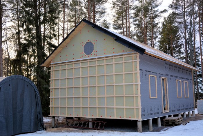 Hus under renovering med klimatskivor och stående läkt på gavel, grundmålad panel monterad på nedre delen.