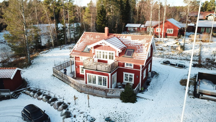 Nybyggt rött hus med snöig trädgård och angränsande byggnader sedd från ovan.