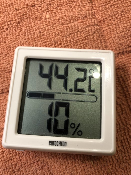 Digital termometer visar 42.2 grader och 18% luftfuktighet på en frottéhandduk.