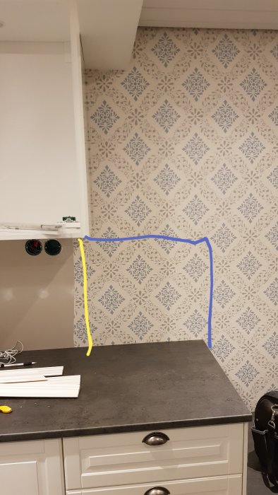 Kökshörn med tapetserad vägg och blåa samt gula markeringar för kakellistposition.