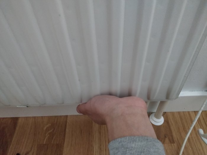 Hand som känner på ett radiatorselement nära ventilen för att bedöma värmen.