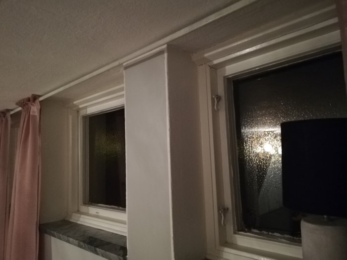 Ett fönster högt upp i ett rum med betongtak, rosa gardiner och en bordslampa, möjlig plats för renovering till hemmabio.