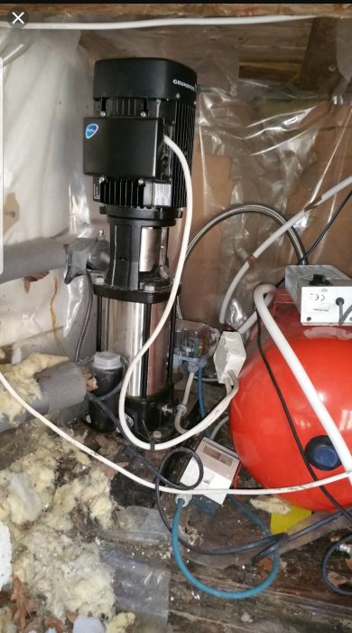 Vattenpump och hydrofor i ett utrymme med isolering och kablar, avstängda i några månader.