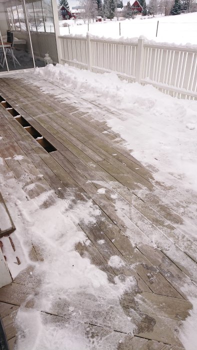 Delvis sopad träaltan med snörester, bredvid en inglasad veranda och med vit staket, på en vinterdag.