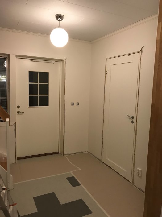 Ny målad hall i kalkvit med borttagna lister runt dörrar och fönster samt omonterad taklampa.