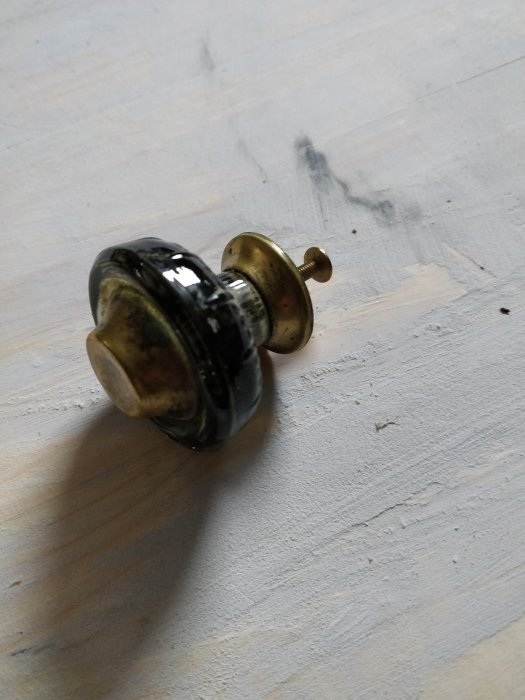En gammaldags mässingsknopp med patina som ligger på ett blekt träunderlag.