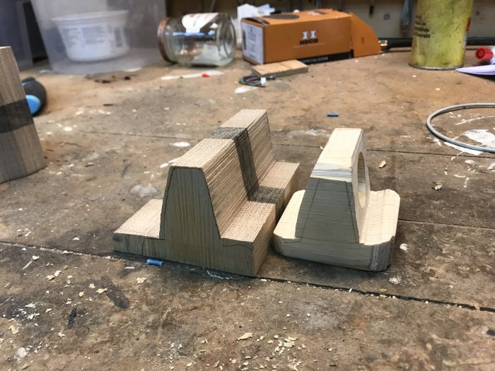 Träblock formade som hållare till Apple Watch-laddare på ett arbetsbord, bredvid bandsågsspån.