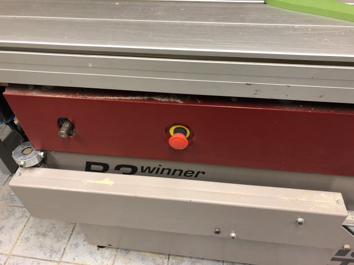 Nödstopp och manöverpanel på en röd "B3 winner" maskin i en verkstad.