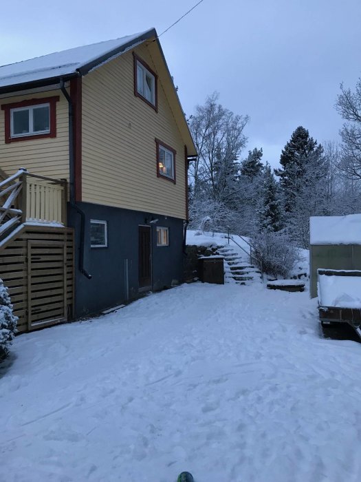 Gult hus med snötäckt mark vid skymning, plats för tänkt utbyggnad syns till höger.