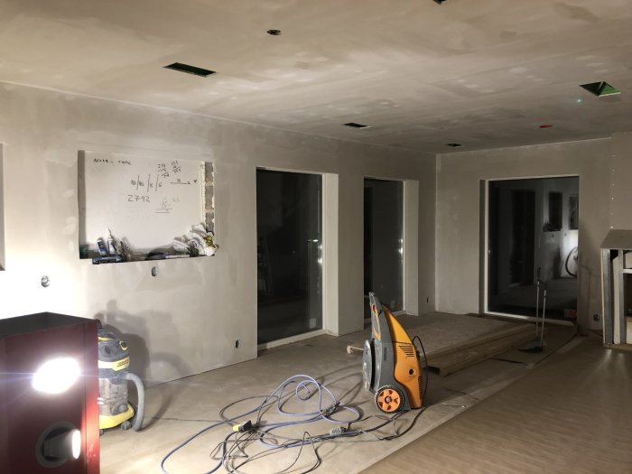 Under renovering, ett oinrett kök med gipsskivor på väggarna, en vit tavla och byggmaterial på golvet.