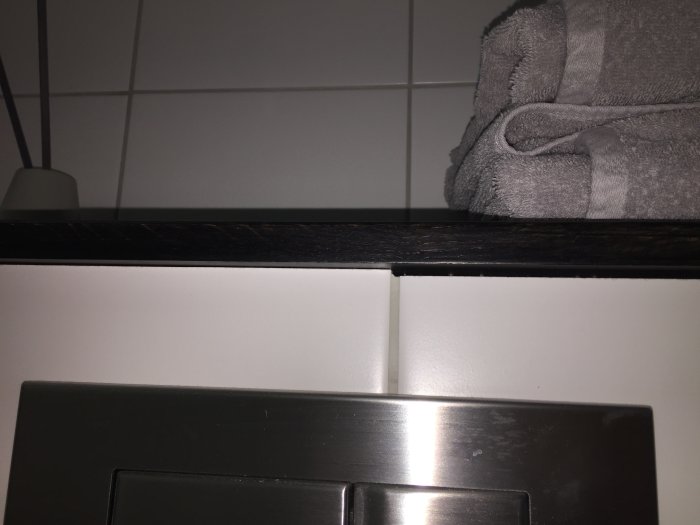 Vägghängd toalett med ojämn kakelkant och löst trälock ovanpå inbyggd cistern.